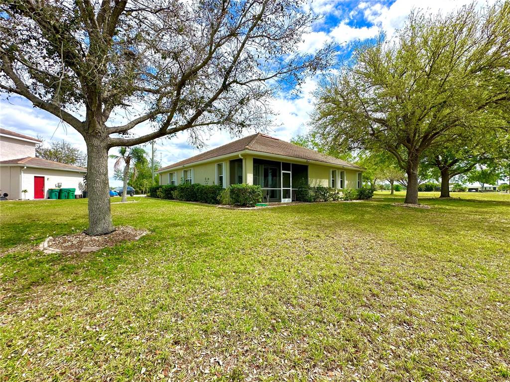 A light-colored house with a screened-in porch sits on a large, grassy lawn — 24479 VIENISON LN, PUNTA GORDA, FL