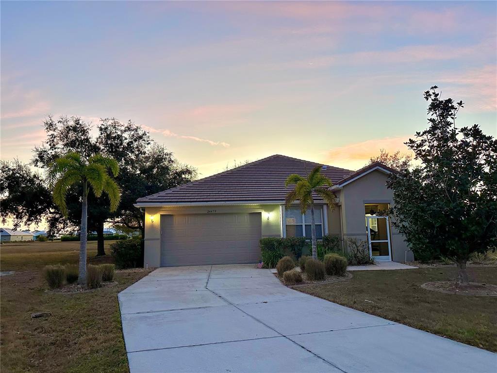 A single-story house with a two-car garage, a concrete driveway, and palm trees at sunset — 24479 VIENISON LN, PUNTA GORDA, FL