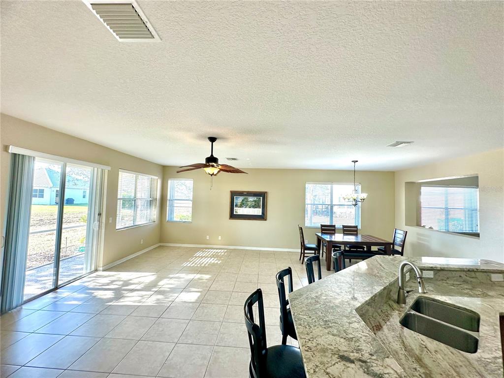 A bright, open-concept living and dining area features tile flooring, a kitchen island, and windows — 24479 VIENISON LN, PUNTA GORDA, FL