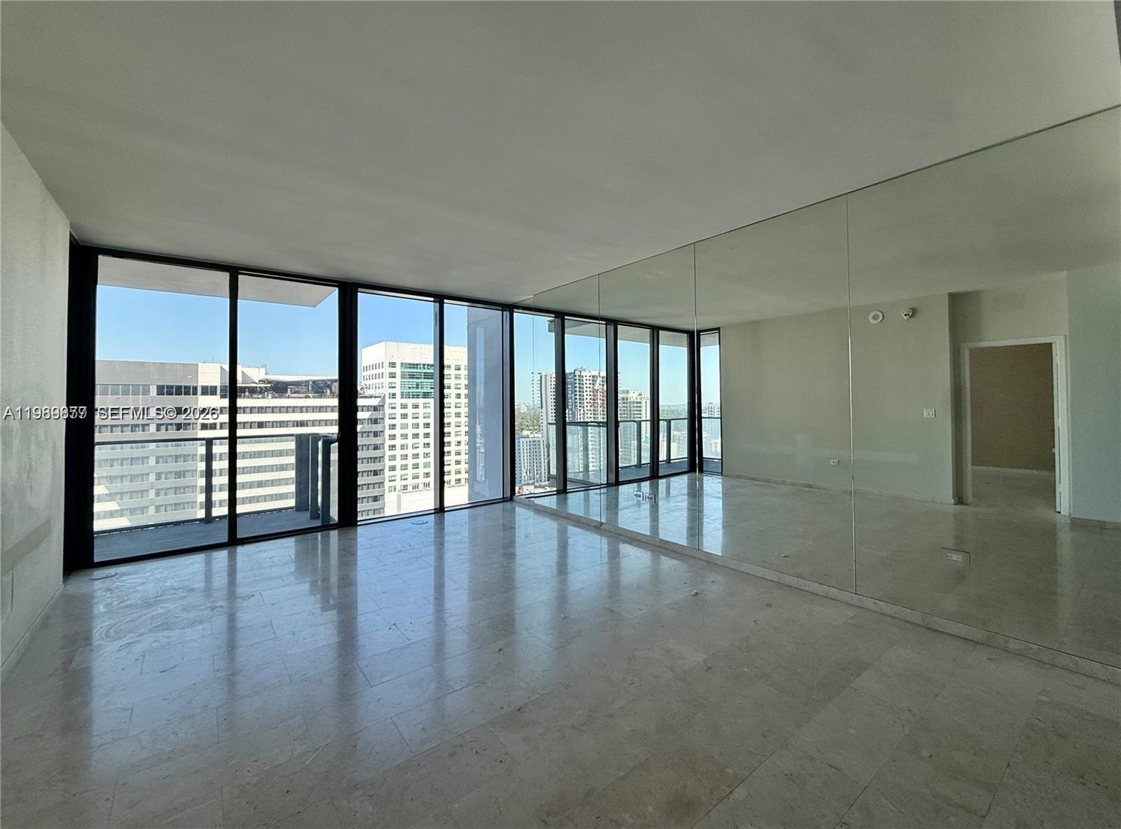 An empty room features marble floors, floor-to-ceiling windows, and a large mirrored wall — 88 SW 7th St # 1808, Miami FL 33130, MIAMI, FL