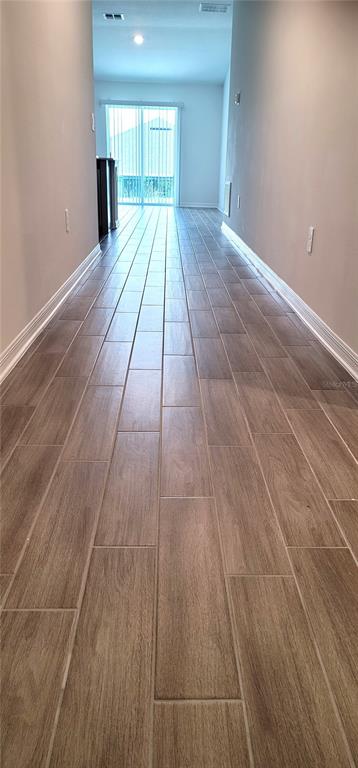 A long hallway with wood-look tile flooring leads toward a sliding glass door — 707 STAFFORA STREET, HAINES CITY, FL
