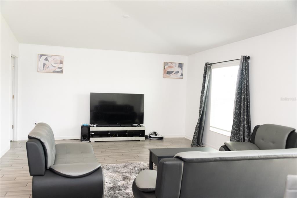 A living room features gray and black sofas, a television on a stand, and tile flooring — 707 STAFFORA STREET, HAINES CITY, FL