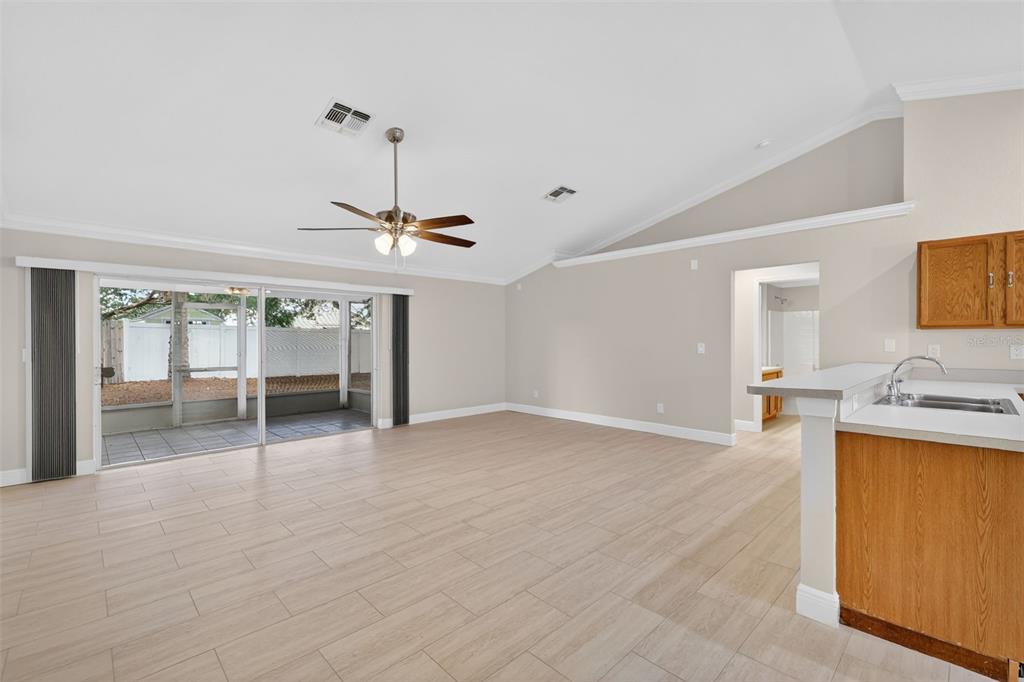 A spacious living room with light tile flooring, vaulted ceilings, and sliding glass patio doors — 2294 KNOLLWOOD DRIVE, LEESBURG, FL