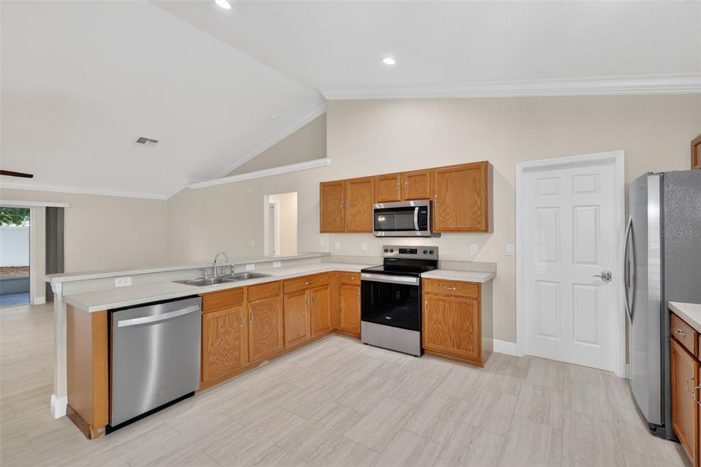 A kitchen with oak cabinets, stainless steel appliances, and light-colored tile flooring — 2294 KNOLLWOOD DRIVE, LEESBURG, FL
