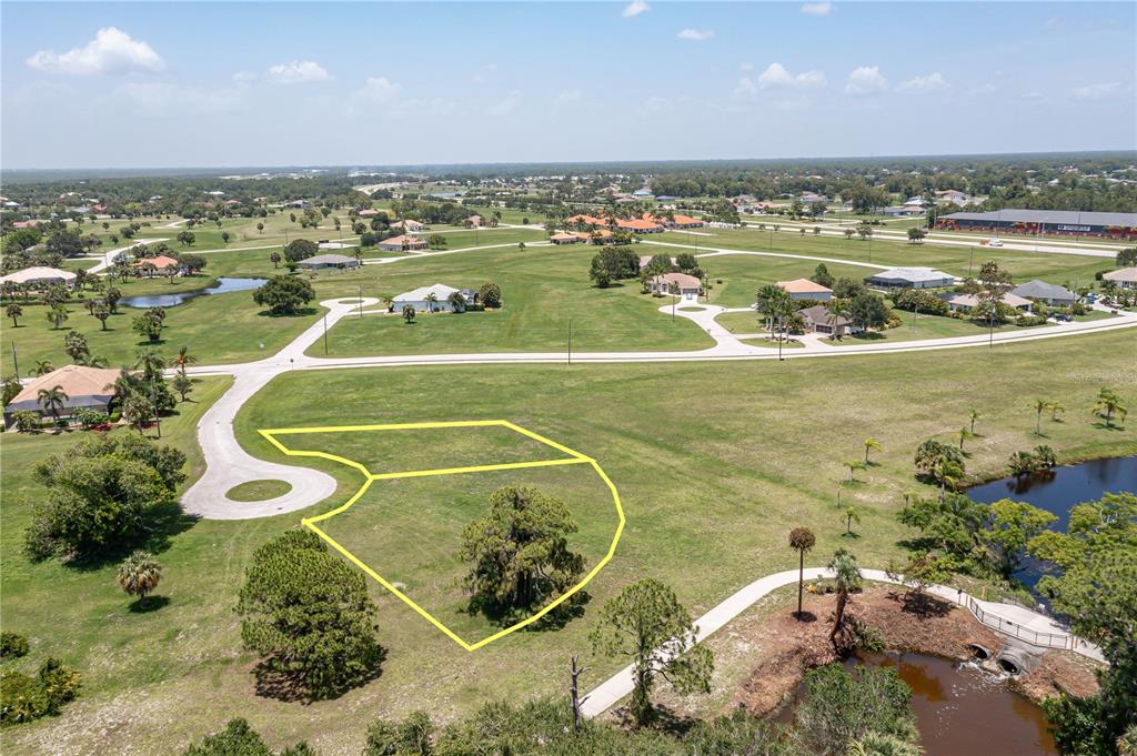 An aerial view shows a vacant residential lot outlined in yellow near a paved road — 16494 TOGAS WAY, PUNTA GORDA, FL