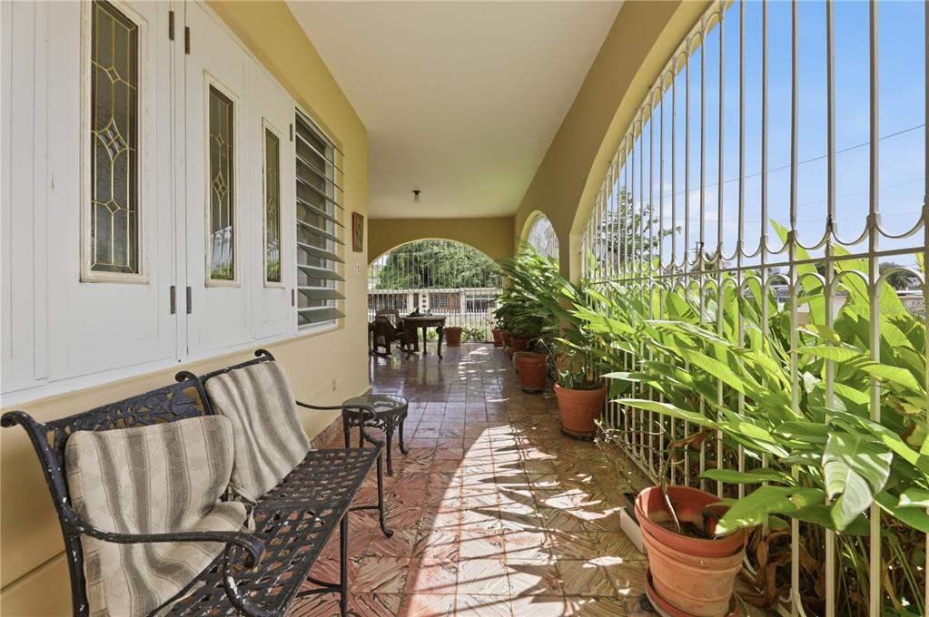 A covered outdoor porch features tiled flooring, a metal bench, potted plants, and security bars — 241 B AVENUE, FAJARDO, PR