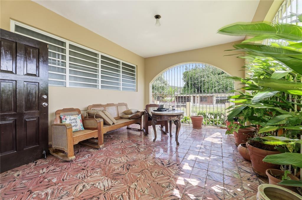 A covered porch features patterned tile flooring, a wooden bench, a small table, and potted plants — 241 B AVENUE, FAJARDO, PR