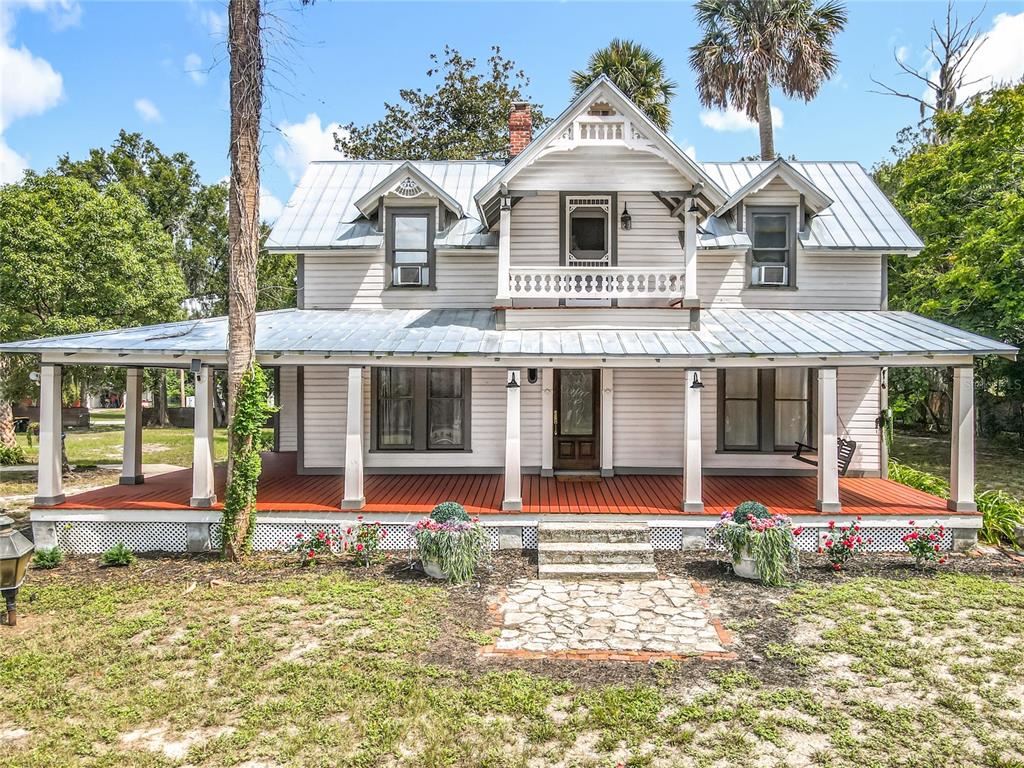 A two-story white house with a metal roof and a large wrap-around front porch — 525 W BLUE SPRINGS AVENUE, ORANGE CITY, FL