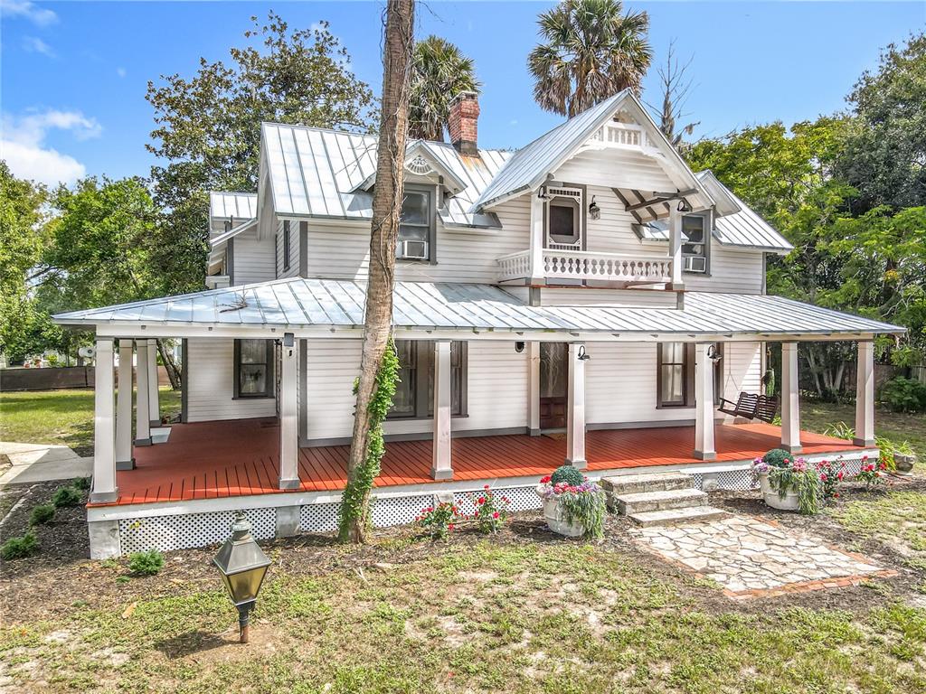 A two-story white farmhouse with a metal roof and a large wrap-around porch — 525 W BLUE SPRINGS AVENUE, ORANGE CITY, FL