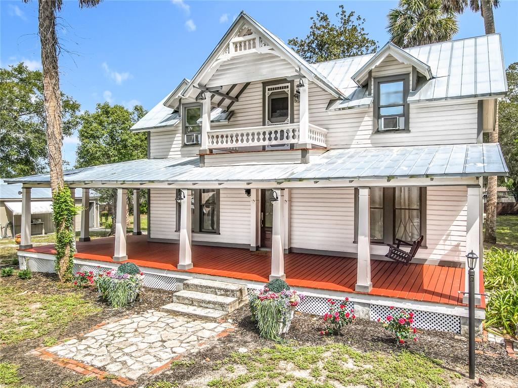 A two-story white farmhouse with a metal roof, wraparound porch, and a second-story balcony — 525 W BLUE SPRINGS AVENUE, ORANGE CITY, FL