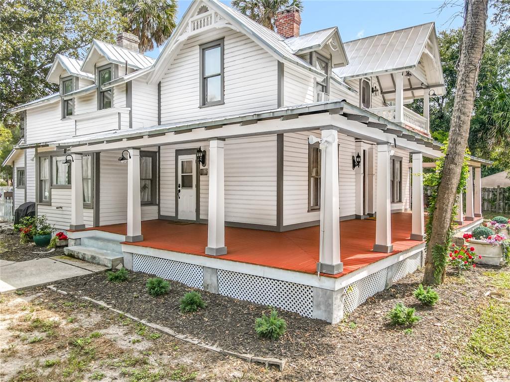 A white two-story house with a wrap-around porch and metal roof stands on a lot — 525 W BLUE SPRINGS AVENUE, ORANGE CITY, FL