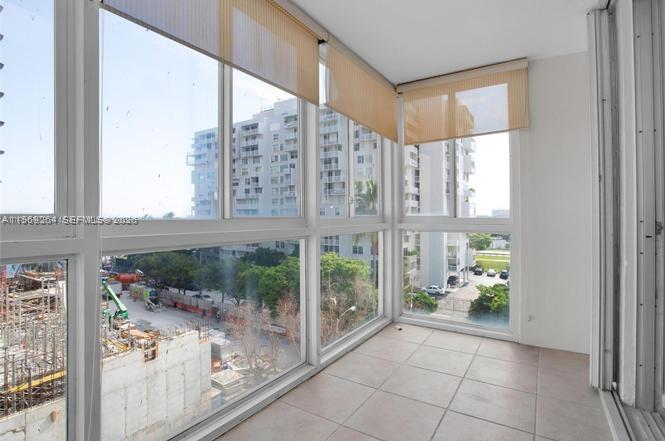 An enclosed balcony with tile flooring, large windows, and tan roller shades overlooking a construction site — 145 SE 25th Rd # 602, Miami FL 33129, MIAMI, FL