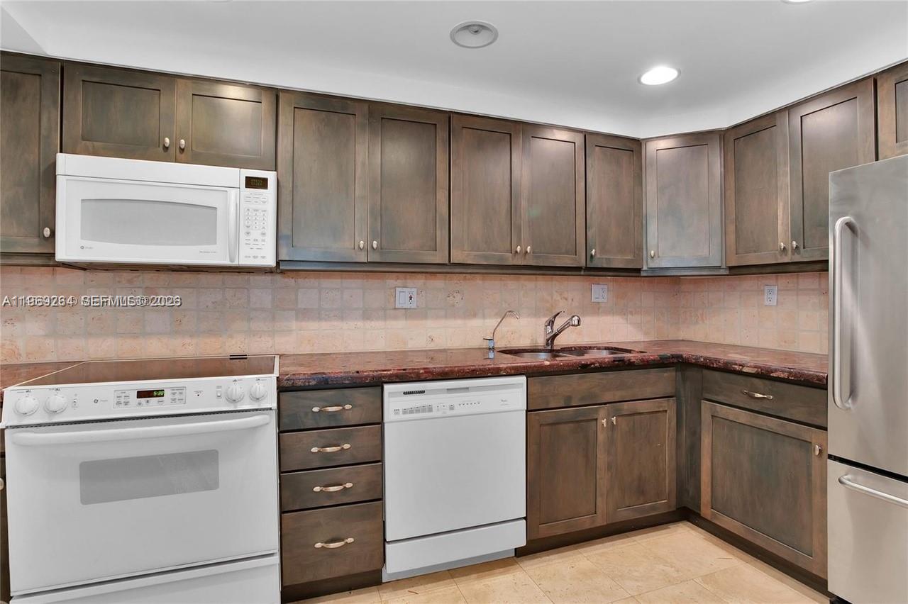 A kitchen features dark wood cabinets, a red granite countertop, and white appliances — 145 SE 25th Rd # 602, Miami FL 33129, MIAMI, FL