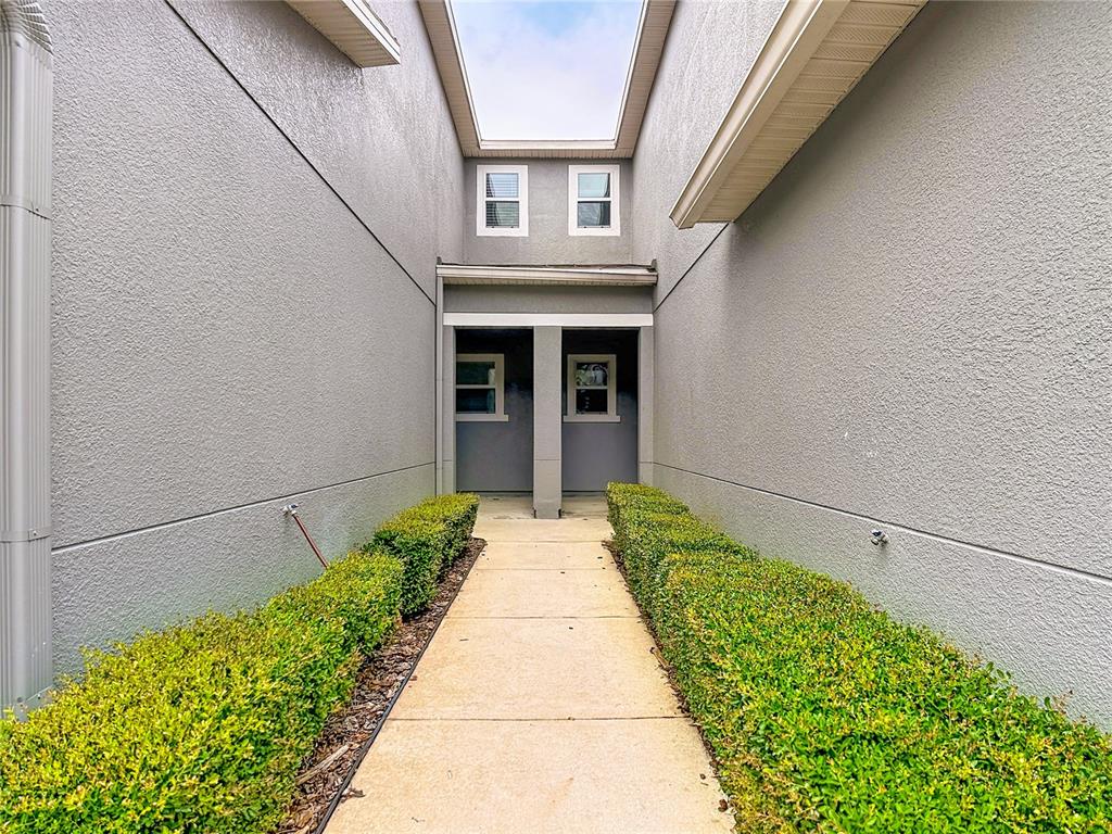 A concrete walkway leads between two gray stucco walls toward a recessed building entrance — 1009 CHALCEDONY STREET, KISSIMMEE, FL