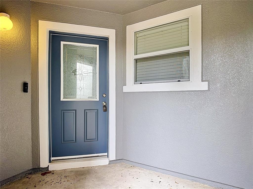 A blue front door with a glass insert sits next to a window on a porch — 1009 CHALCEDONY STREET, KISSIMMEE, FL