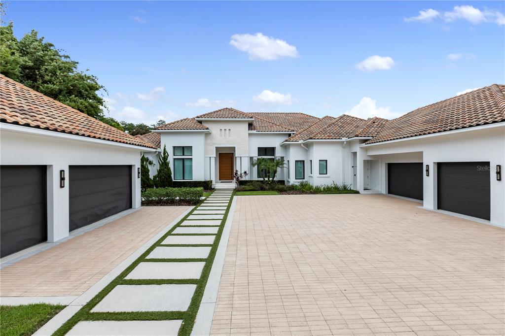 A modern house exterior features a paved courtyard, two garages, and a central entryway — 6149 GROSVENOR SHORE DR, WINDERMERE, FL