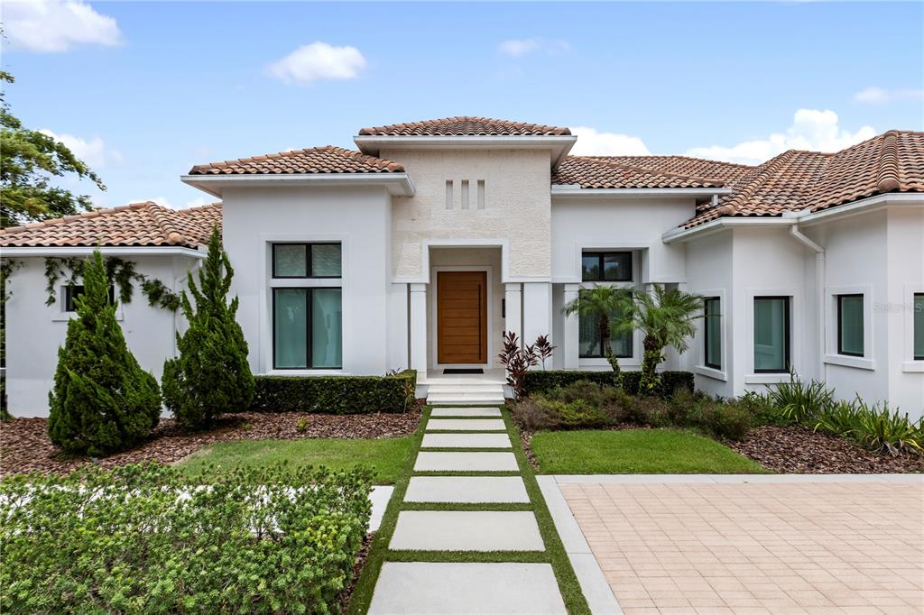A modern white house with a tile roof, wooden front door, and stone walkway — 6149 GROSVENOR SHORE DR, WINDERMERE, FL