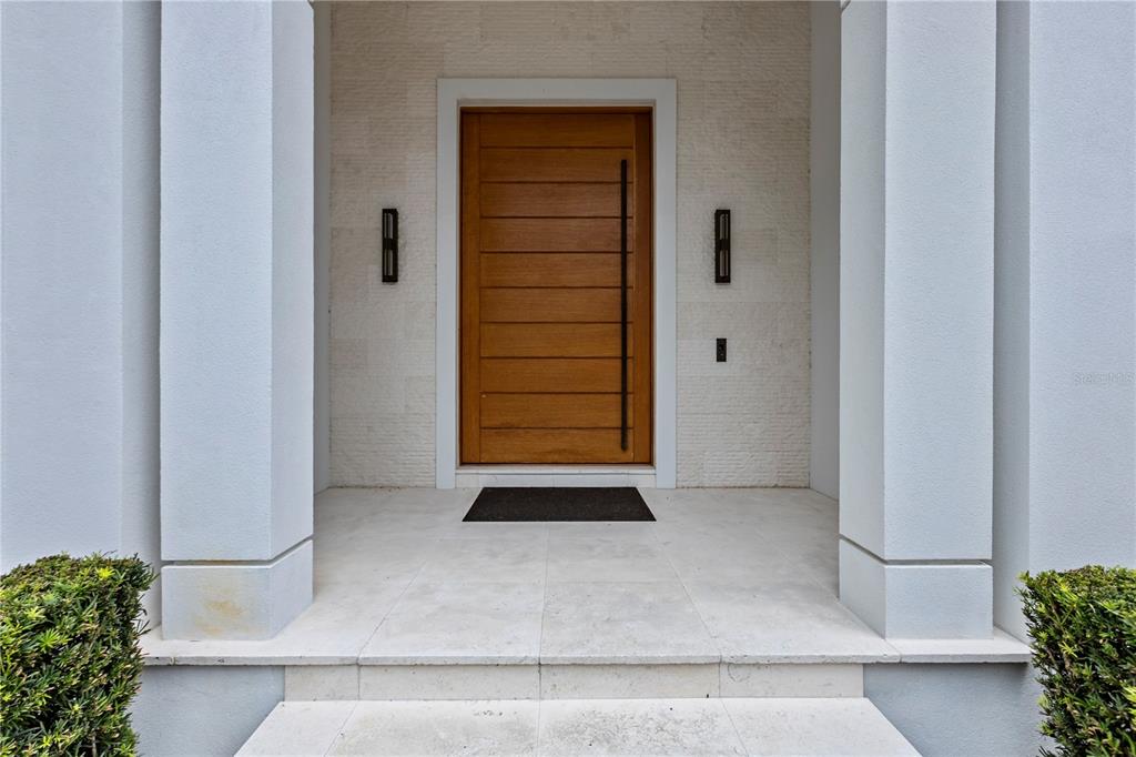A modern wooden front door is centered between two white pillars on a stone porch — 6149 GROSVENOR SHORE DR, WINDERMERE, FL