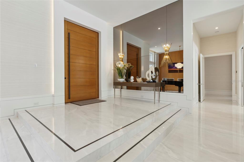 A modern entryway features a raised marble floor, a wooden door, and a large wall mirror — 6149 GROSVENOR SHORE DR, WINDERMERE, FL