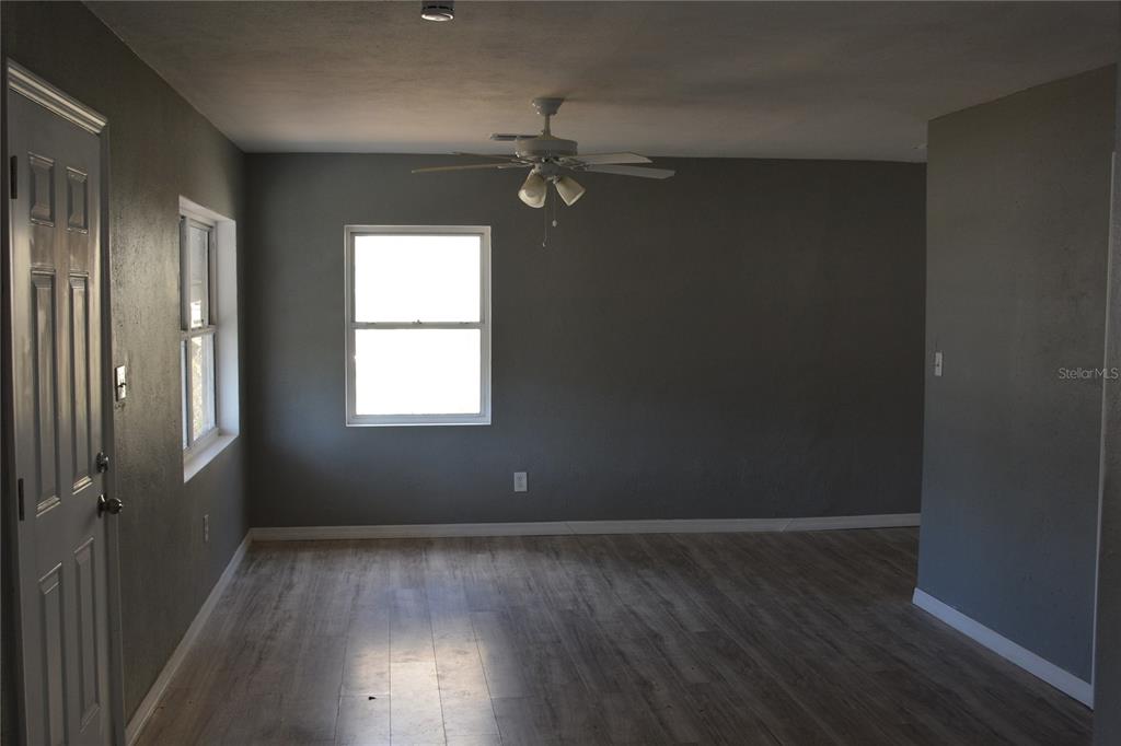 An empty room features gray walls, light wood-look flooring, a ceiling fan, and two windows — 1328 3RD STREET NE, WINTER HAVEN, FL