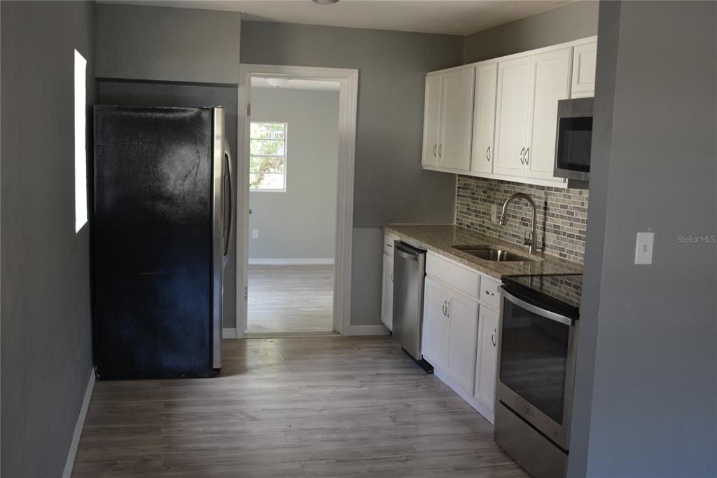 A kitchen features white cabinets, stainless steel appliances, a tiled backsplash, and light wood flooring — 1328 3RD STREET NE, WINTER HAVEN, FL