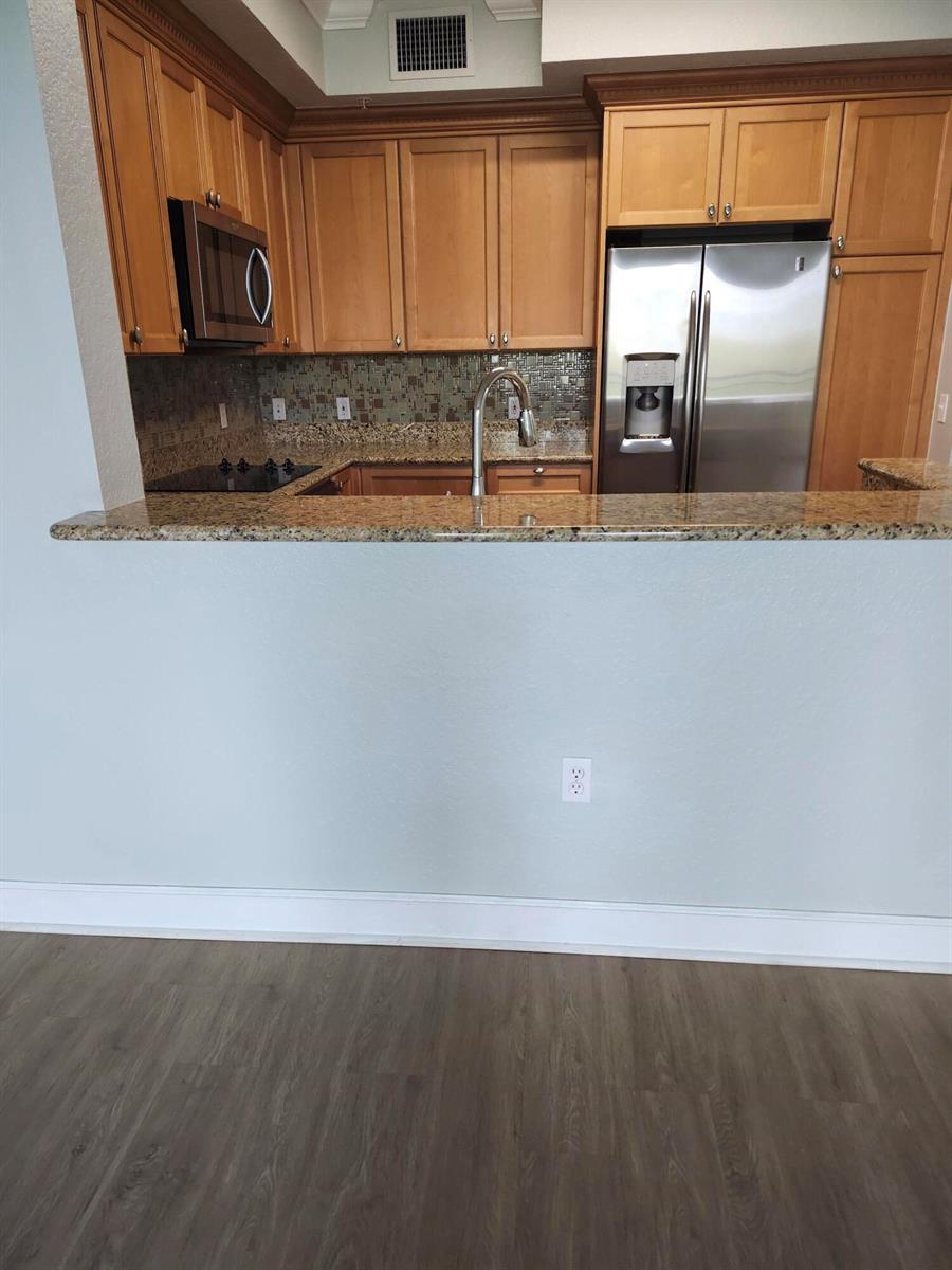 A kitchen features wood cabinets, granite countertops, stainless steel appliances, and a breakfast bar — 1660 Renaissance Commons Boulevard # 2504, Boynton Beach FL 33426, BOYNTON BEACH, FL