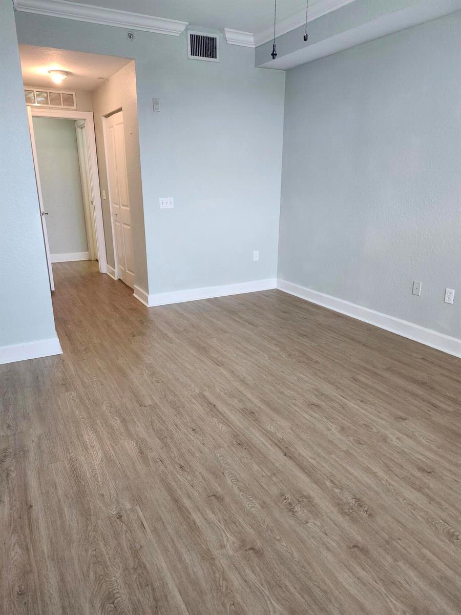 An empty room with light blue walls, wood-look flooring, and a doorway leading to a hallway — 1660 Renaissance Commons Boulevard # 2504, Boynton Beach FL 33426, BOYNTON BEACH, FL