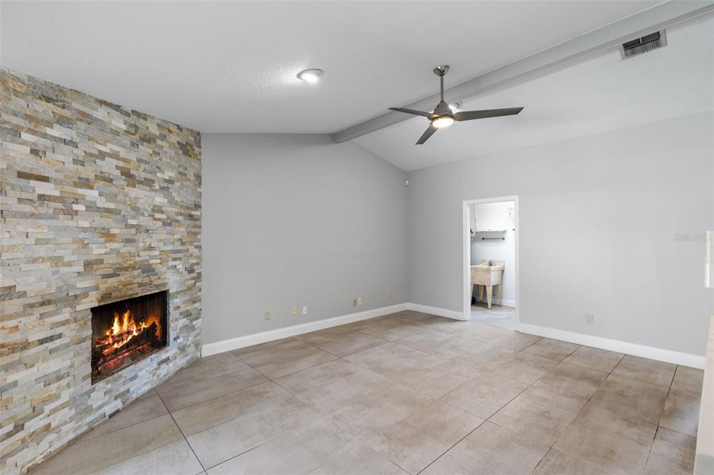 A living room features a stone fireplace, gray walls, tile flooring, and a ceiling fan — 351 NEEDLES TRAIL, LONGWOOD, FL