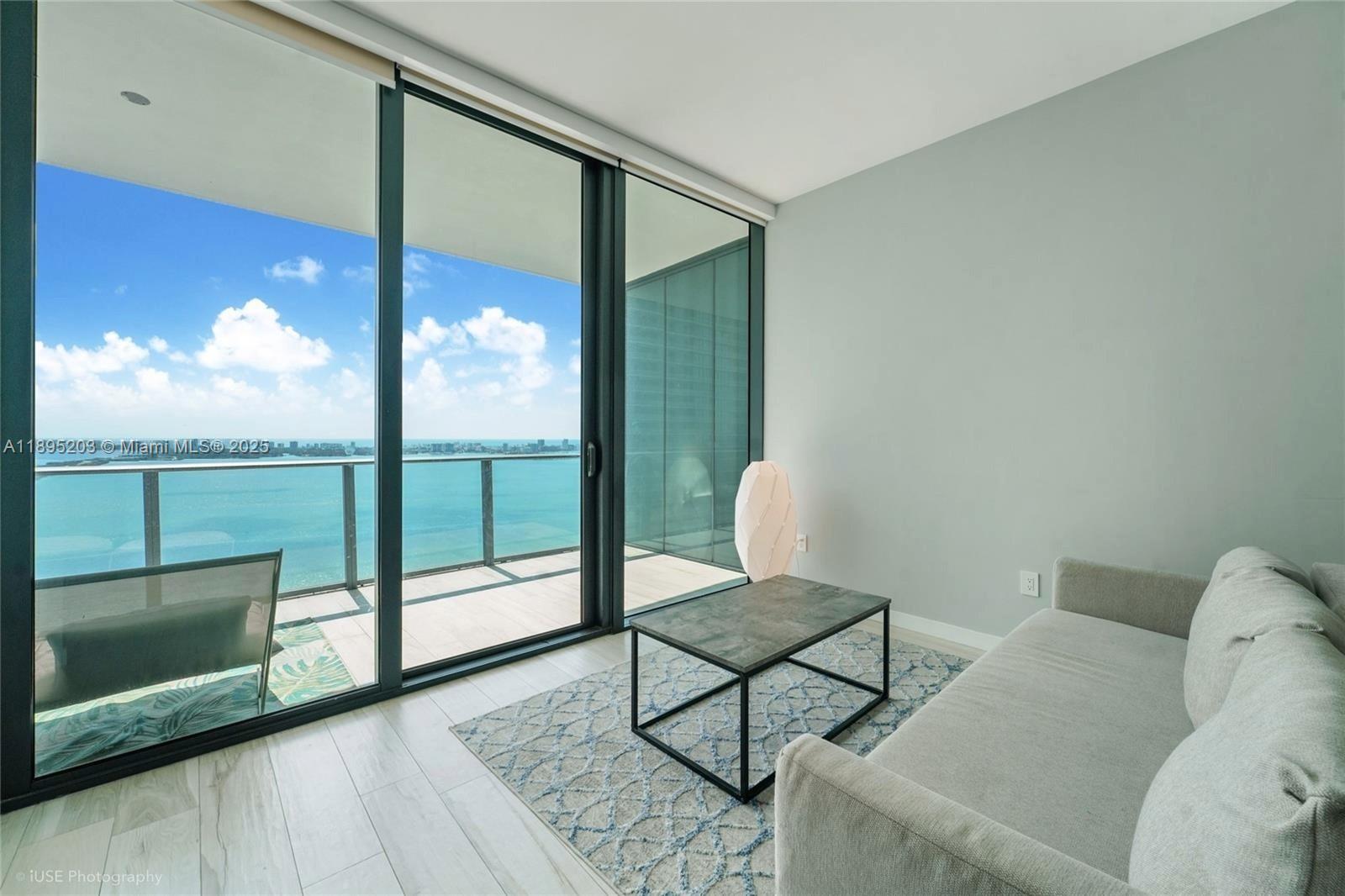 A living room features a light gray sofa, a coffee table, and a balcony overlooking water — 480 NE 31st St # 4106, Miami FL 33137, MIAMI, FL