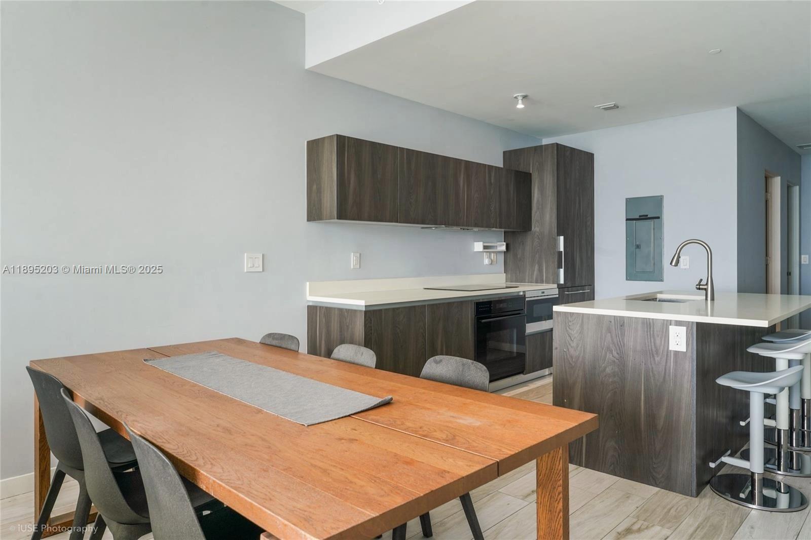 A modern kitchen features dark wood cabinetry, a central island with bar stools, and a dining table — 480 NE 31st St # 4106, Miami FL 33137, MIAMI, FL