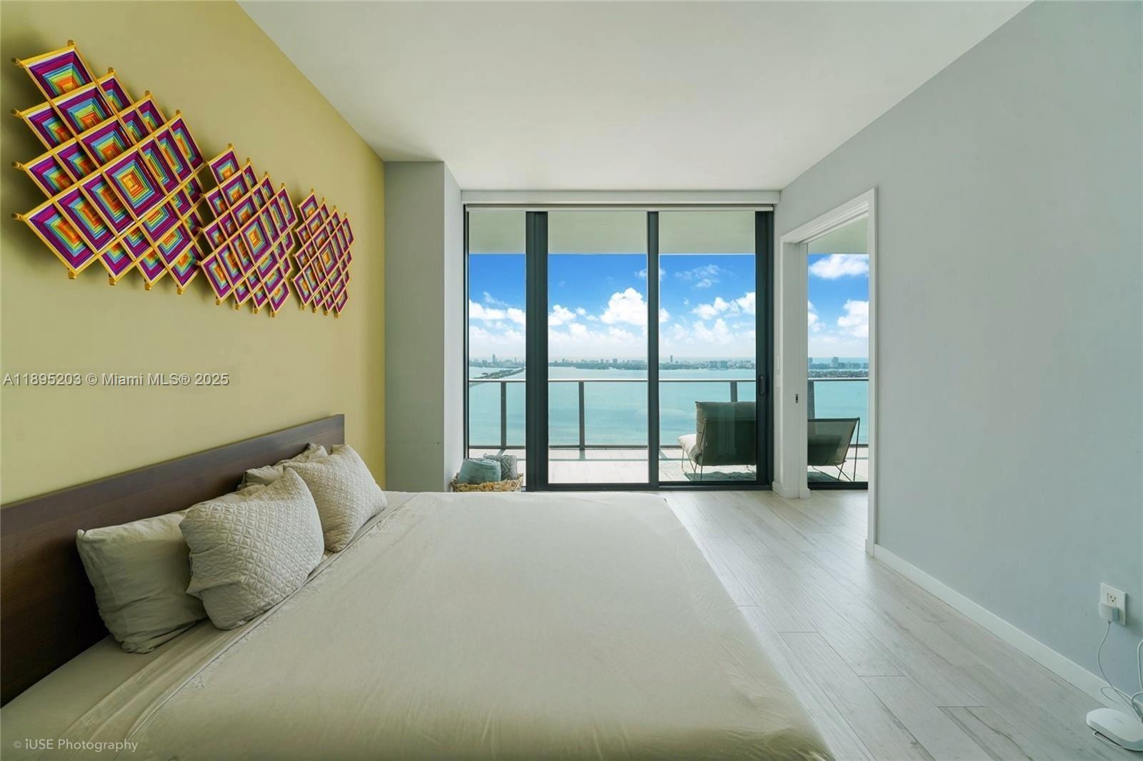 A bedroom features a large bed, colorful wall art, and floor-to-ceiling windows overlooking the ocean — 480 NE 31st St # 4106, Miami FL 33137, MIAMI, FL