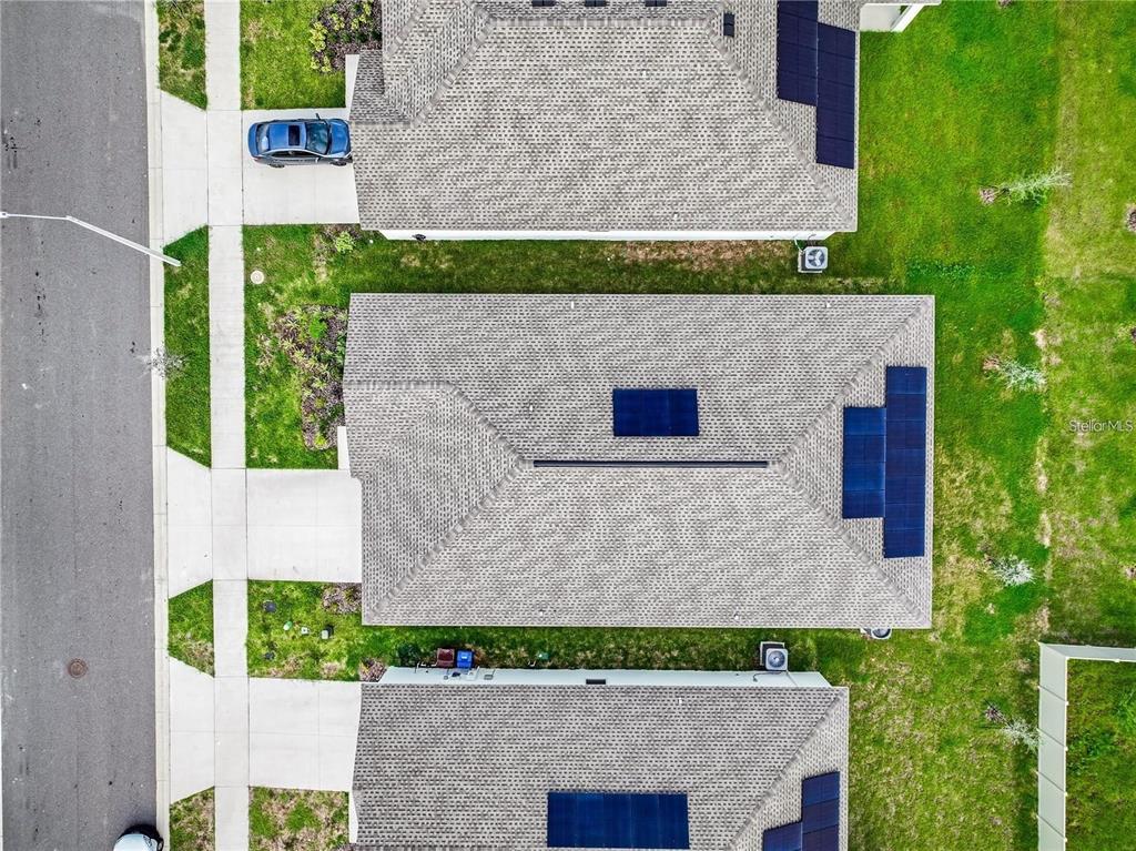 An aerial view shows three suburban houses with shingled roofs and installed solar panels — 664 TANARO LANE, HAINES CITY, FL