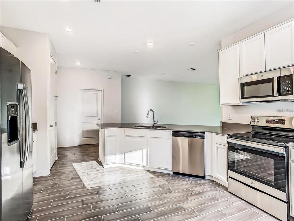 A kitchen features stainless steel appliances, white cabinetry, dark countertops, and wood-look tile flooring — 664 TANARO LANE, HAINES CITY, FL