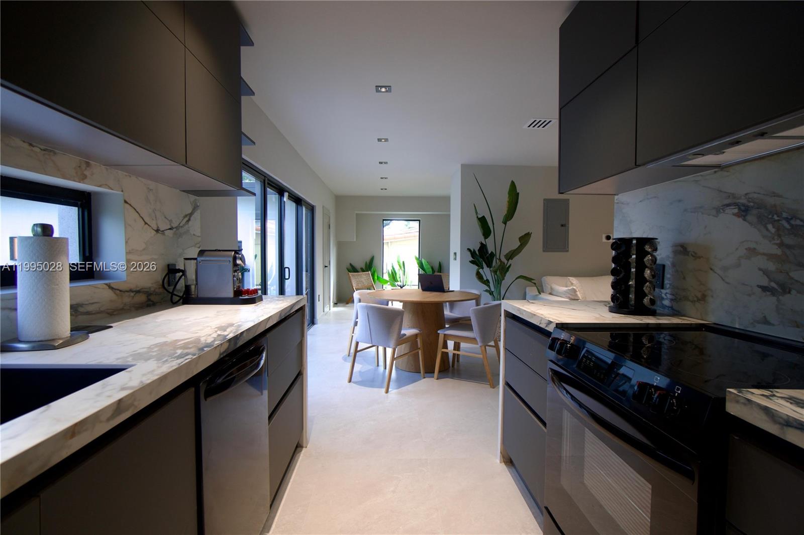 A modern kitchen features dark cabinetry, marble countertops, and a view into a dining area — 2155 SW 25th Ter, Miami FL 33133, MIAMI, FL