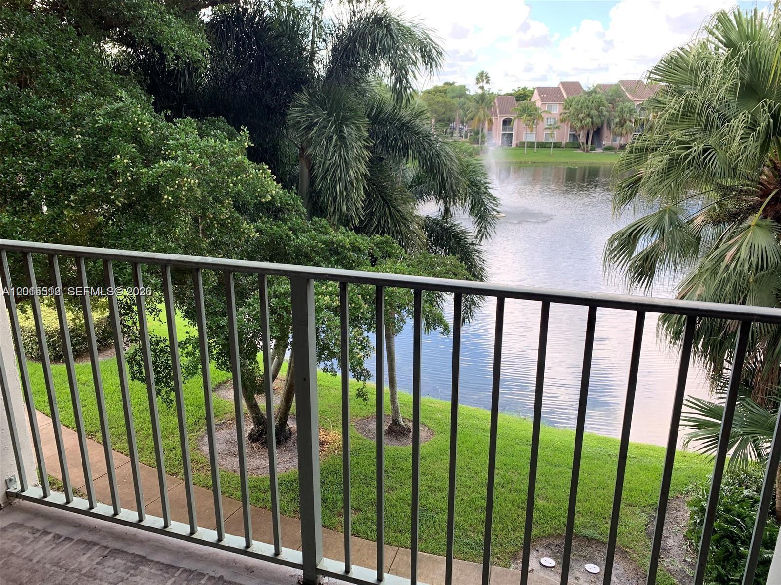 A balcony view overlooking a lake with a fountain, palm trees, and apartment buildings — 12118 Saint Andrews Pl # 304, Miramar FL 33025, MIRAMAR, FL