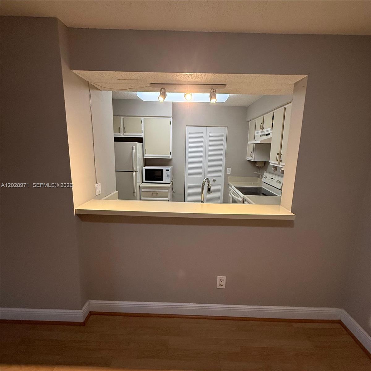 A kitchen with white cabinets and appliances is viewed through a rectangular wall cutout — POMPANO BEACH, FL