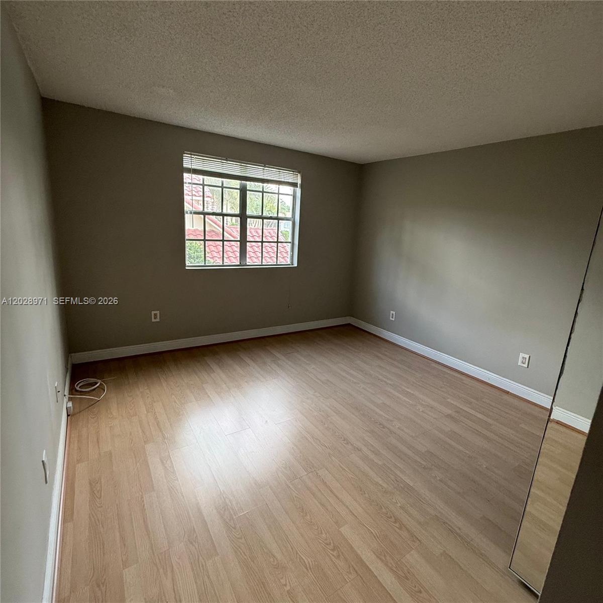 An empty bedroom features light wood-look laminate flooring, beige walls, and a single window — POMPANO BEACH, FL