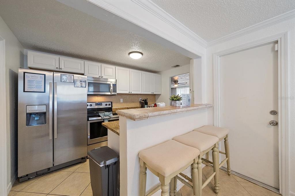 A kitchen features white cabinets, stainless steel appliances, a tiled breakfast bar, and three stools — 2135 LEE LANE, SARASOTA, FL