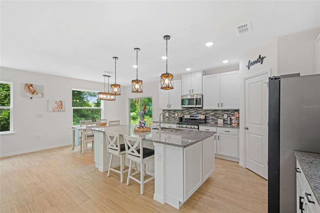 A kitchen features white cabinets, granite countertops, a center island with seating, and pendant lighting — 1137 BRADFORD RIDGE DRIVE, LEESBURG, FL