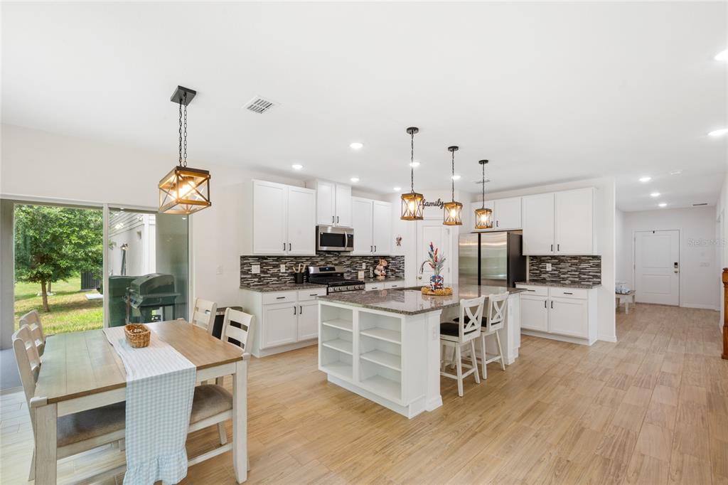 A kitchen features white cabinetry, a granite-topped island, pendant lighting, and light wood flooring — 1137 BRADFORD RIDGE DRIVE, LEESBURG, FL