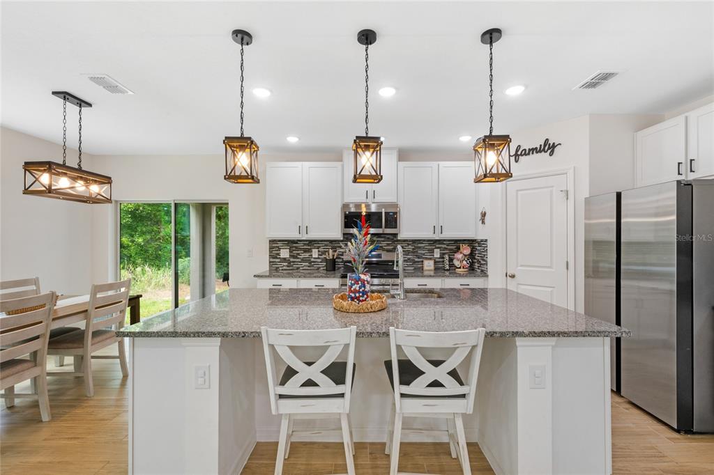 A kitchen features a granite-topped island, white cabinetry, stainless steel appliances, and pendant lighting — 1137 BRADFORD RIDGE DRIVE, LEESBURG, FL