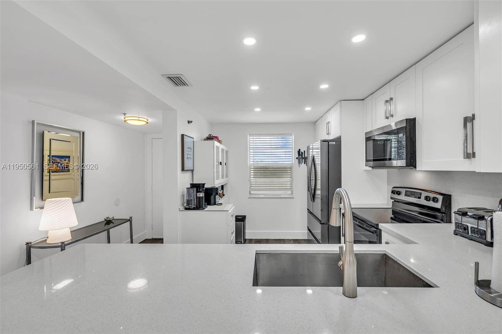 A modern kitchen features white cabinetry, quartz countertops, stainless steel appliances, and recessed lighting — 3910 Inverrary Blvd # B, Lauderhill FL 33319, LAUDERHILL, FL