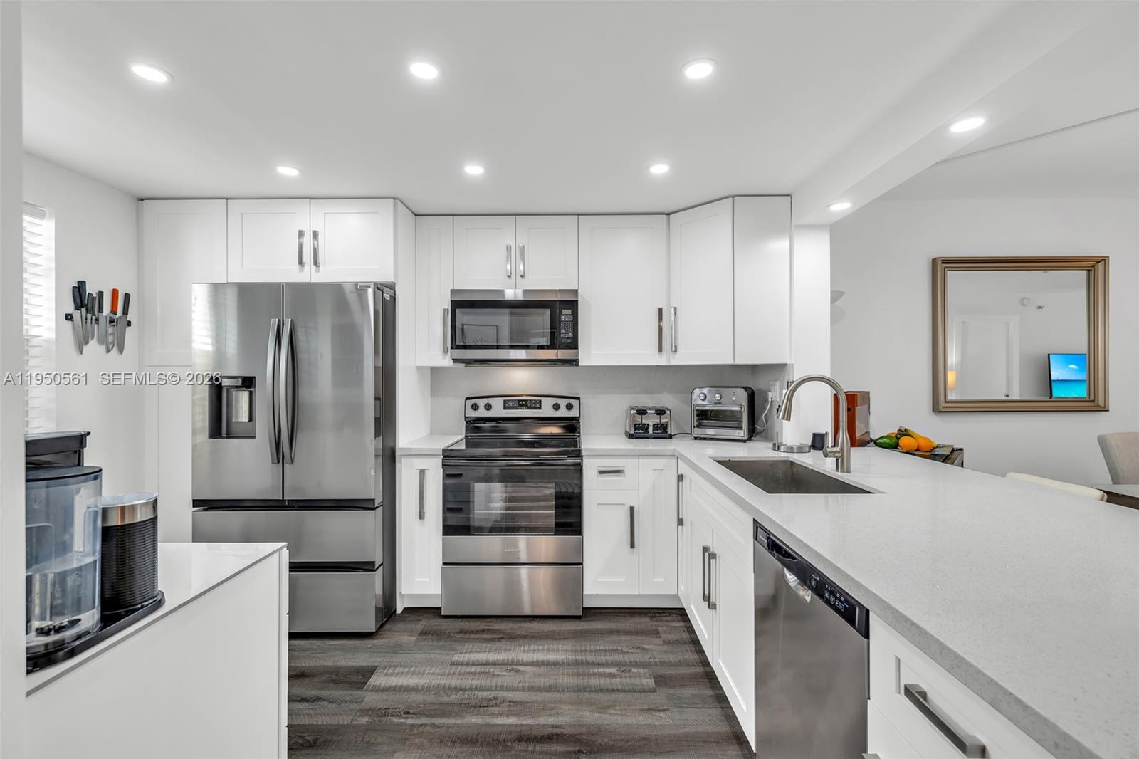 A modern kitchen features white cabinets, stainless steel appliances, and dark wood-look flooring — 3910 Inverrary Blvd # B, Lauderhill FL 33319, LAUDERHILL, FL