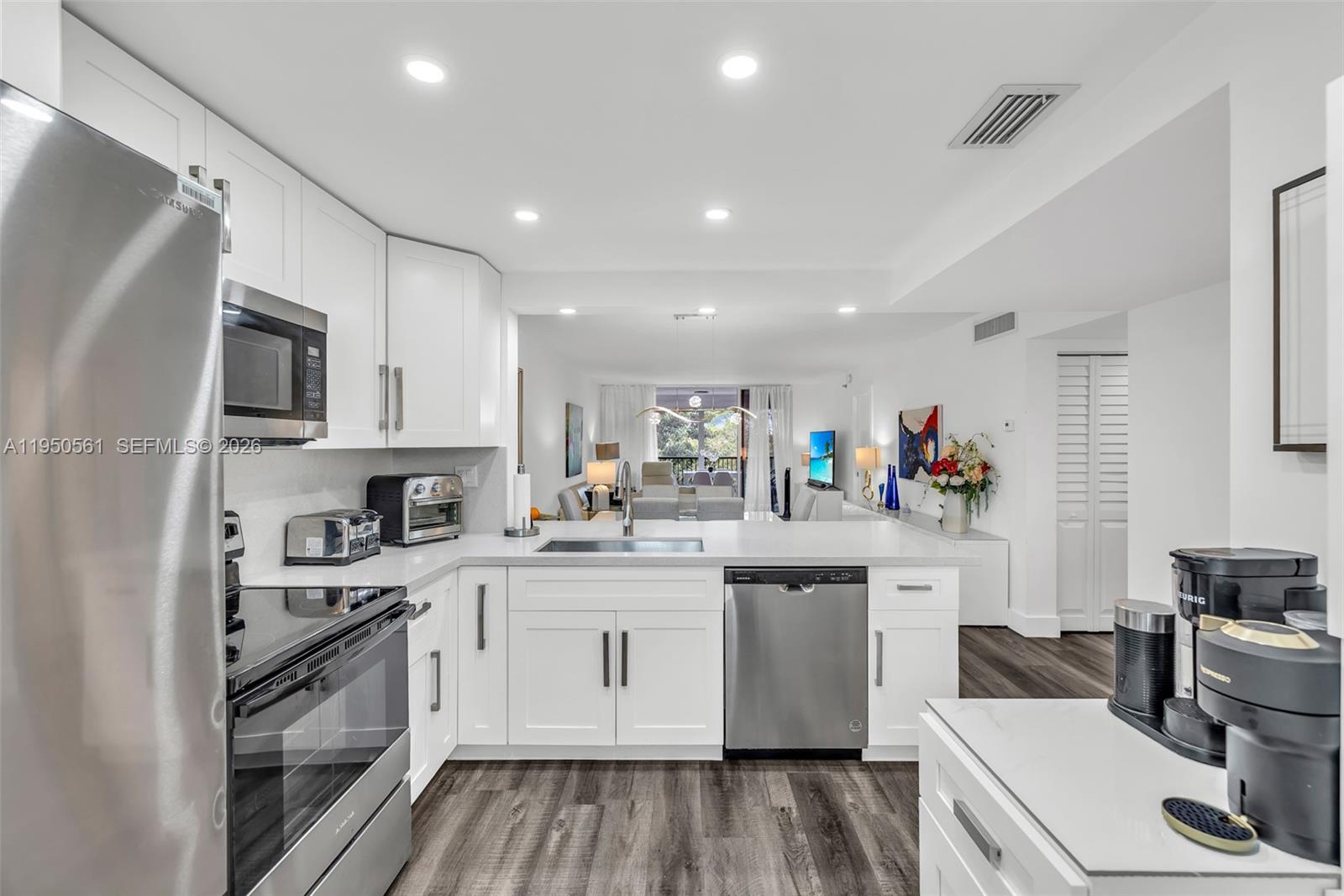 A modern kitchen features white cabinetry, stainless steel appliances, and a view into the living area — 3910 Inverrary Blvd # B, Lauderhill FL 33319, LAUDERHILL, FL