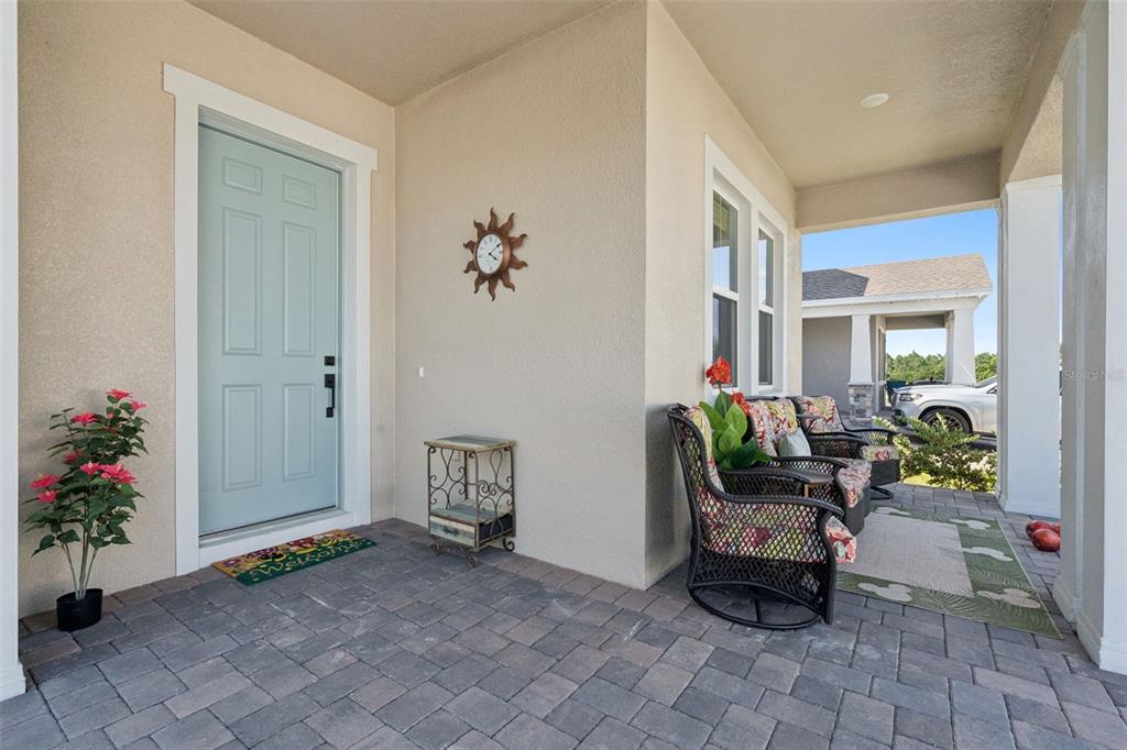 A covered front porch features a light blue door, stone pavers, and outdoor seating — 15652 GENTLE RAIN DRIVE, WINTER GARDEN, FL
