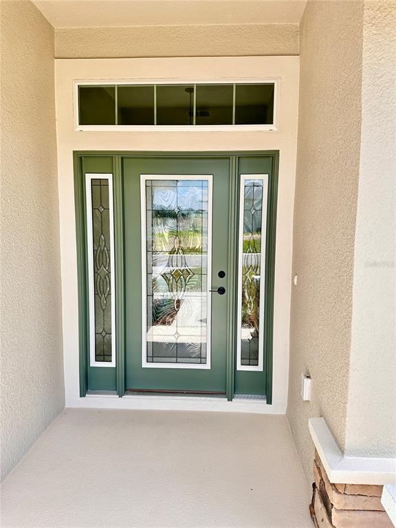 A green front door with glass panels and a transom window sits on a porch — 4493 NE 31ST PLACE, OCALA, FL