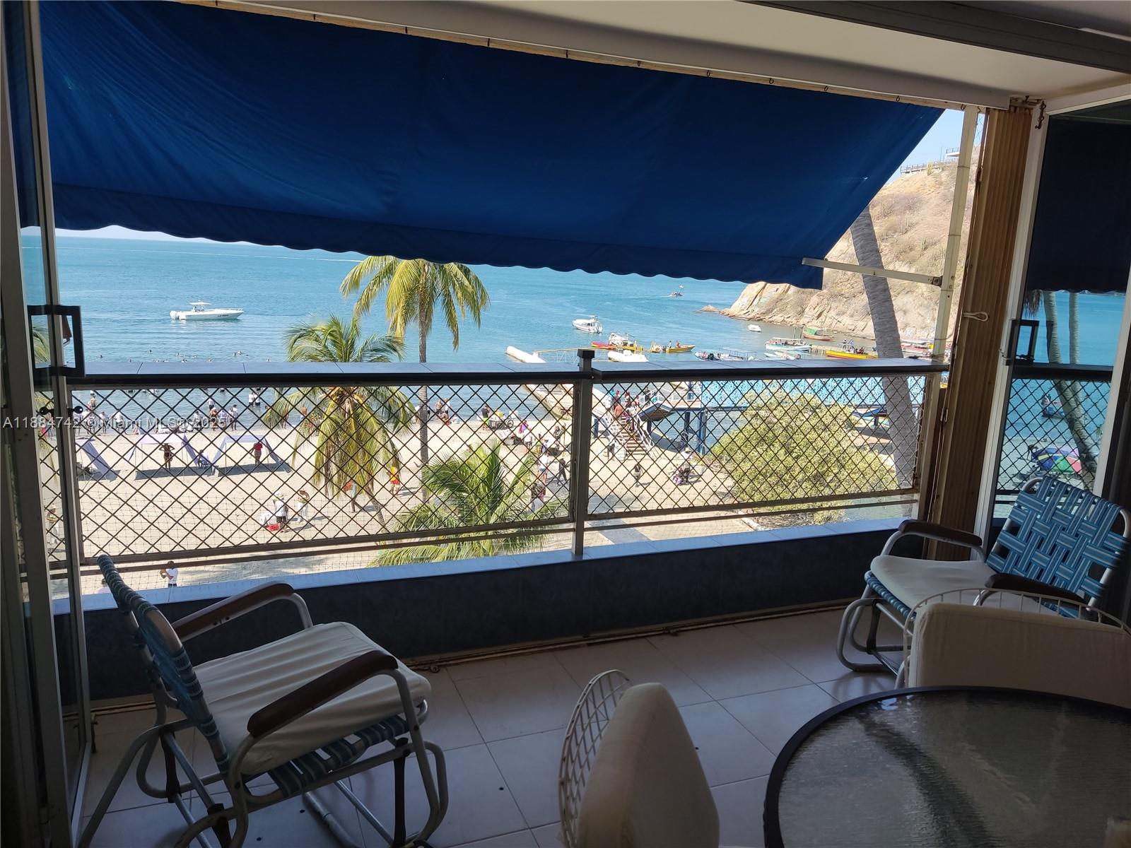 A balcony with outdoor furniture overlooks a beach, ocean, and boats under a blue awning — Carrera 1a # 5-06, SA 130001, SA