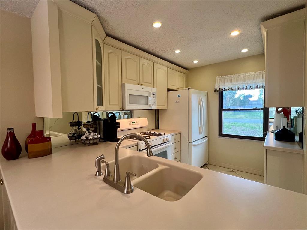 A kitchen features white cabinets, light countertops, a double sink, and a window — 1395 MISSION DRIVE W UNIT 28C, CLEARWATER, FL