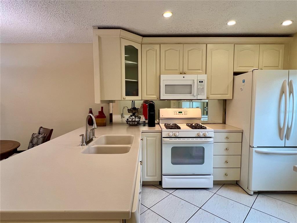 A kitchen features cream-colored cabinets, white appliances, a double sink, and a tiled floor — 1395 MISSION DRIVE W UNIT 28C, CLEARWATER, FL