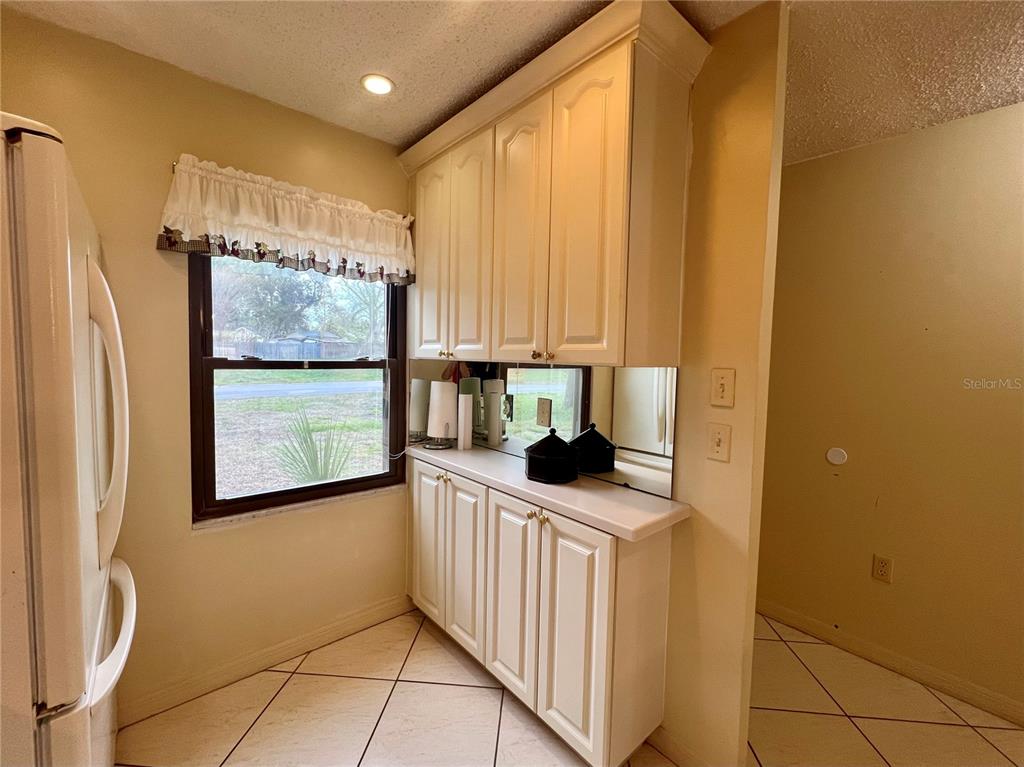 A kitchen features white cabinetry, a mirrored backsplash, and light-colored tile flooring — 1395 MISSION DRIVE W UNIT 28C, CLEARWATER, FL
